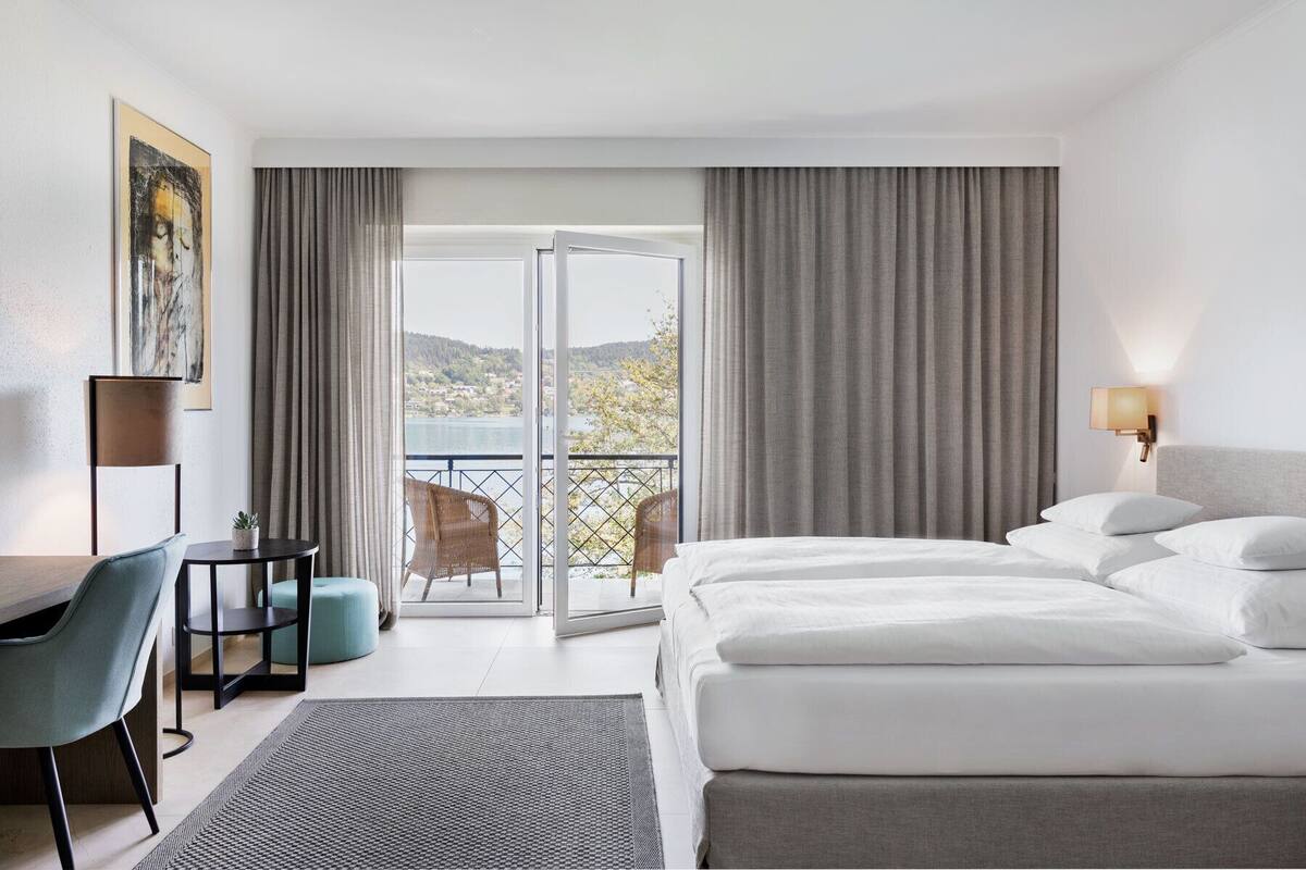 Ein Hotelzimmer mit Bett, Schreibtisch, Stuhl und Blick auf einen See und Hügel.