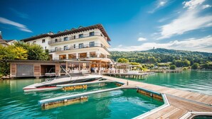 A lakeside hotel with a dock, a boat, and a view of the lake and hills. - Hotel Linde (Maria Woerth)