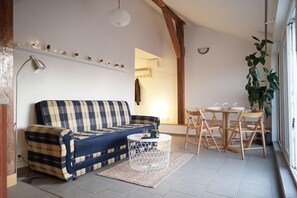 Uma sala de estar acolhedora, com um sofá azul e branco em padrão xadrez, uma mesa de centro branca e um espaço de jantar com cadeiras e mesa de madeira.