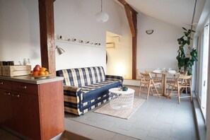 Uma sala de estar aconchegante com sofá, mesa de jantar com cadeiras e bancada na cozinha com frutas.