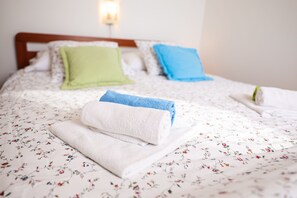 A neatly made bed with floral bedding, pillows, and folded towels. - Luton Apartments, Zadar - Kozino, Heated Pool & Hot Tub (Zadar)