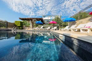 A swimming pool with lounge chairs and umbrellas, surrounded by a stone wall and a building with a tiled roof. - Luton Apartments, Zadar - Kozino, Heated Pool & Hot Tub (Zadar)