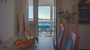 Een eetgedeelte met een tafel gedekt voor twee personen, een fruitmand en uitzicht op de zee door een open deur.