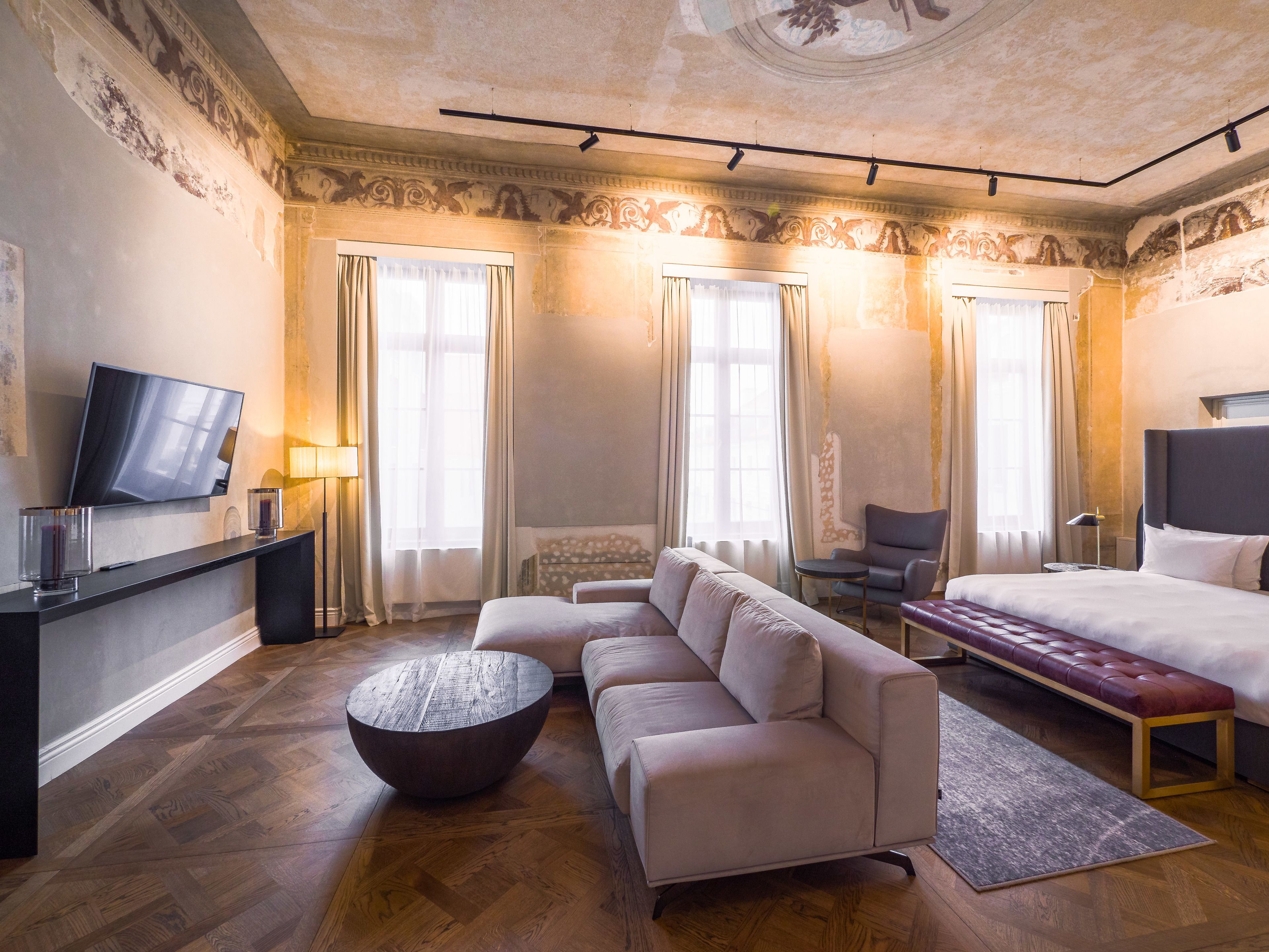 Una habitación de hotel moderna con sofá, una mesa redonda de centro, cama, televisión y una silla.