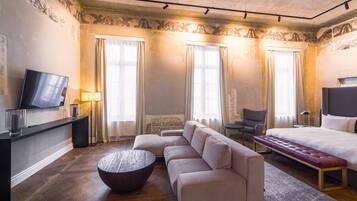 Una habitación de hotel moderna con sofá, una mesa redonda de centro, cama, televisión y una silla.