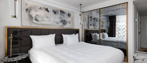 A modern hotel room with a large bed, a side table, a large abstract painting, and a mirrored wardrobe.