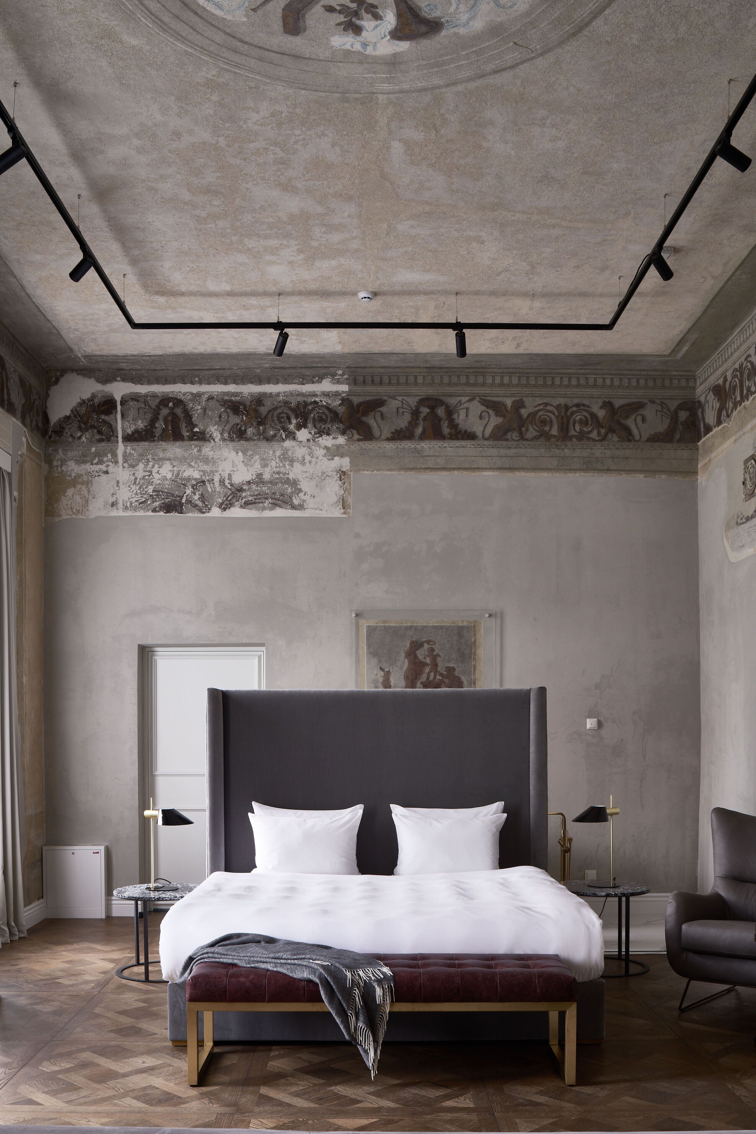 A modern bedroom with a large bed, a bench, a chair, and a small table.