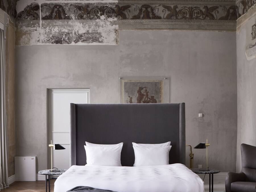 A modern bedroom with a large bed, a bench, a chair, and a small table.