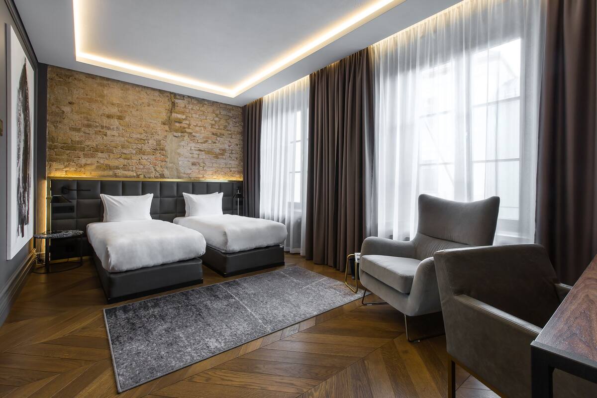 A modern hotel room with a brick accent wall, a large bed, a sofa, and a desk.