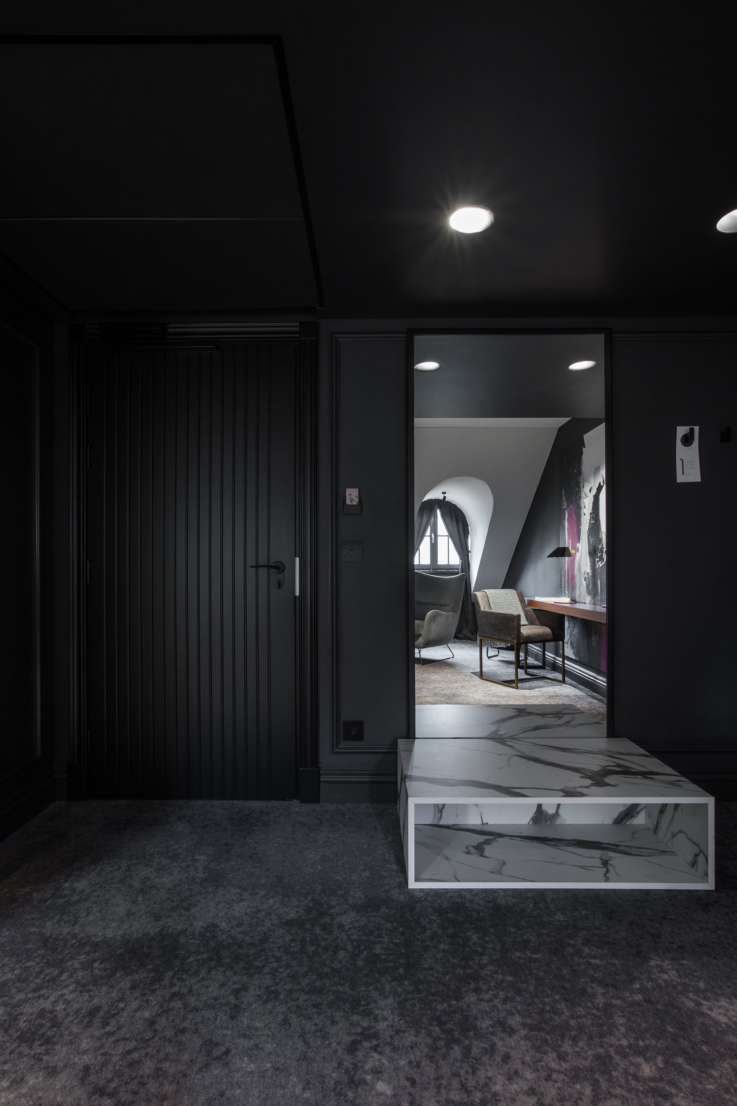 Una habitació moderna amb una porta fosca, una taula de cafè de marbre i una cadira.