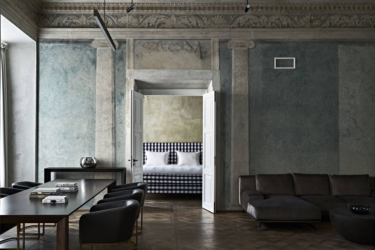 A room with a long table, several chairs, a sofa, and a bed with a checkered headboard.