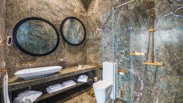A modern bathroom with a marble wall, a large sink, two round mirrors, a glass-enclosed shower, and neatly folded towels.