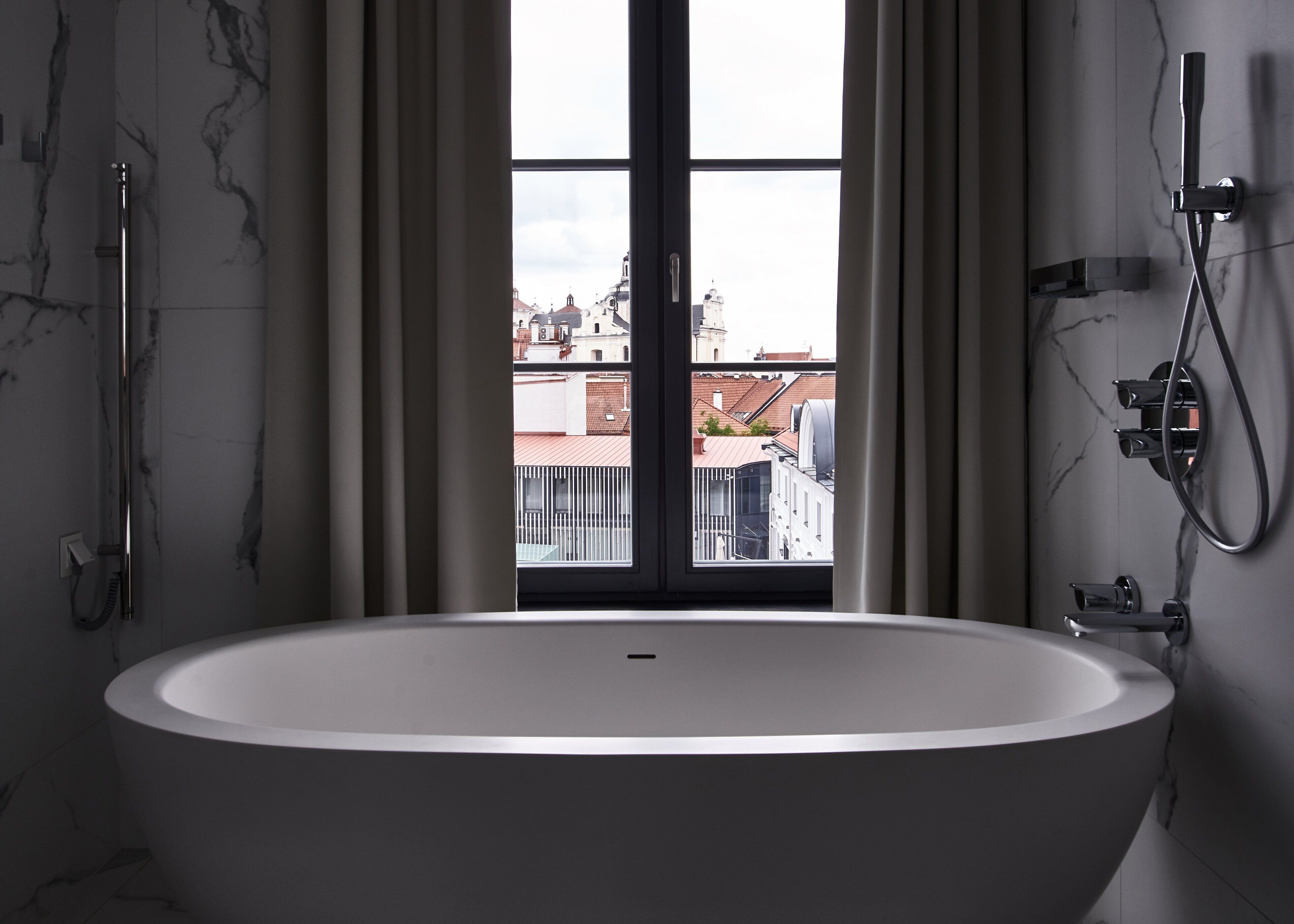 A modern bathroom with a freestanding bathtub, a shower, and a view of buildings through a large window.