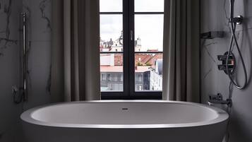 A modern bathroom with a freestanding bathtub, a shower, and a view of buildings through a large window.