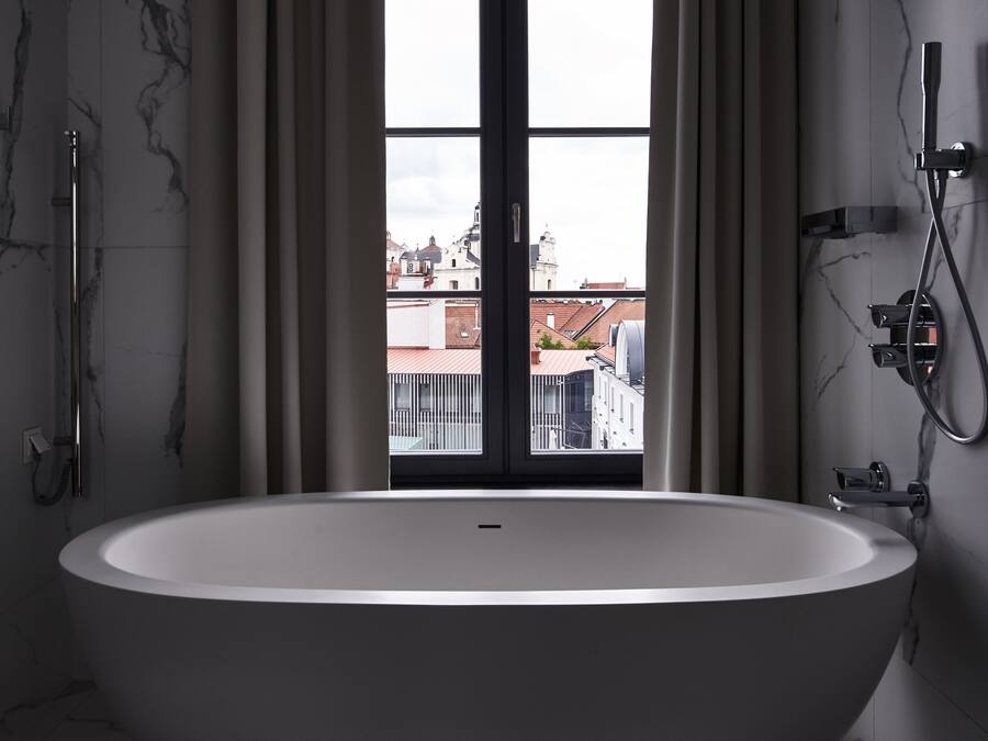 A modern bathroom with a freestanding bathtub, a shower, and a view of buildings through a large window.