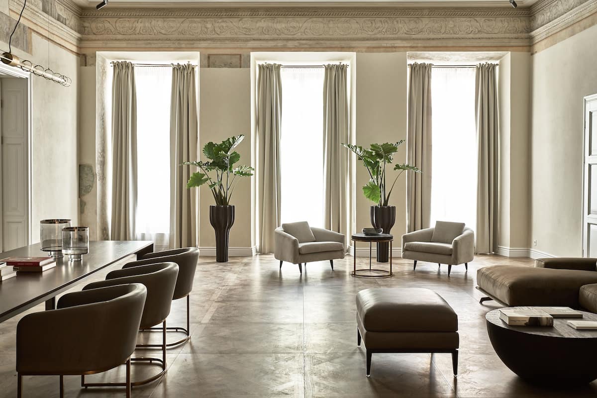 A spacious living room with a large wooden floor, a sofa, two armchairs, a coffee table, and a dining area with chairs and a table.