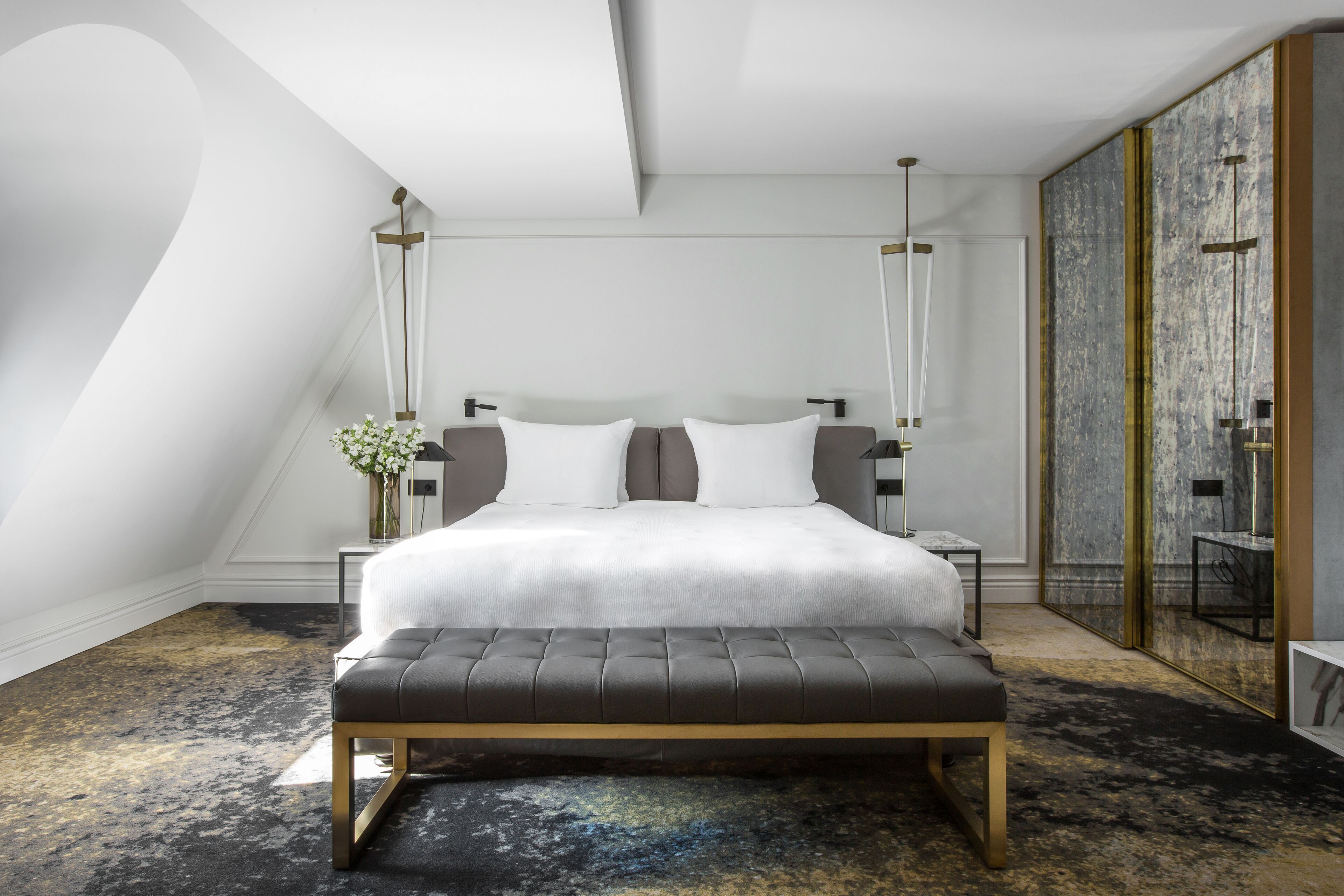 A modern bedroom with a large bed, bedside tables, a bench, and a decorative vase.