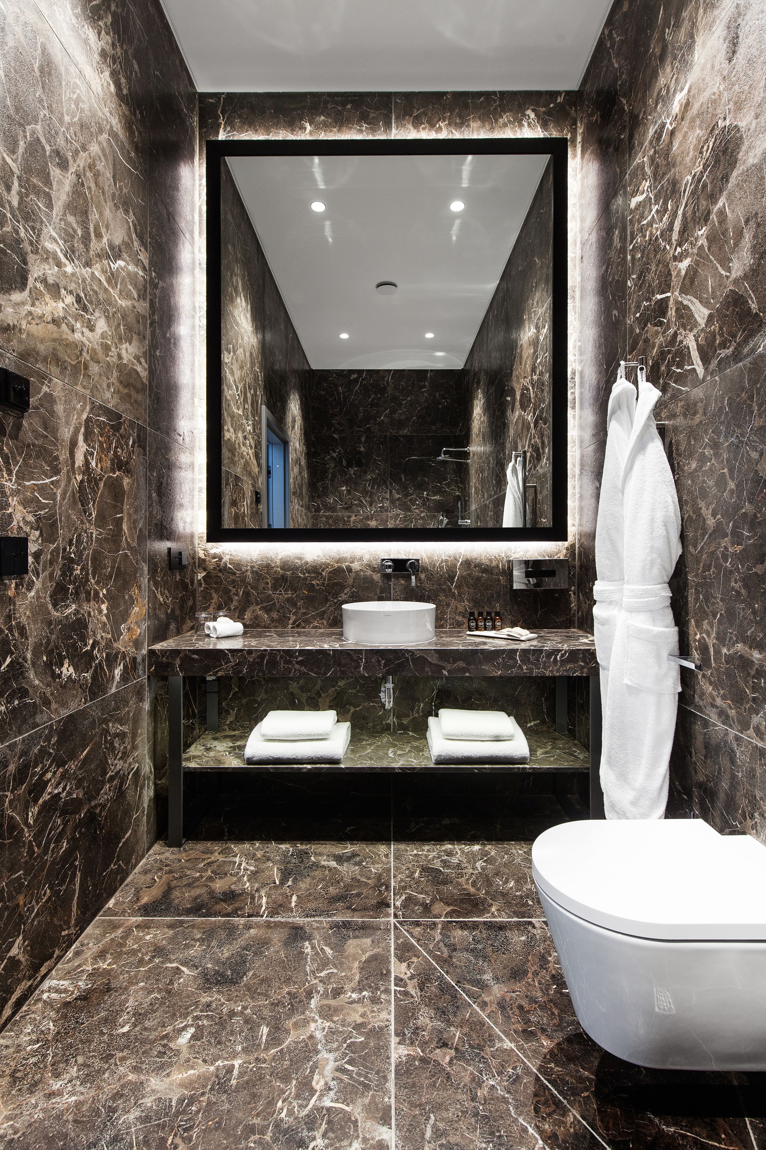 A modern bathroom with a marble sink, a large mirror, and a white toilet.