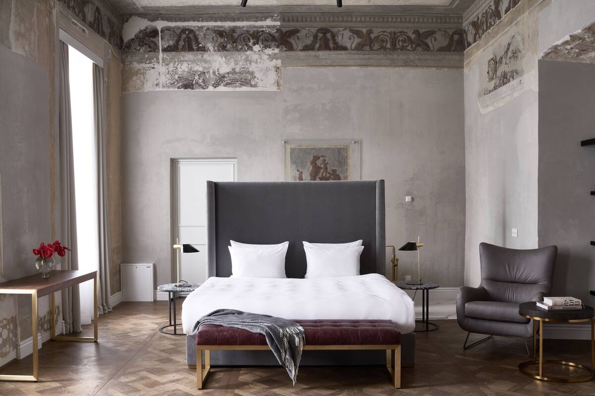 A modern bedroom with a large bed, a chair, a small table, and a nightstand.
