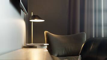 A modern room with a wooden table, a black leather chair, a floor lamp, and a window with curtains.