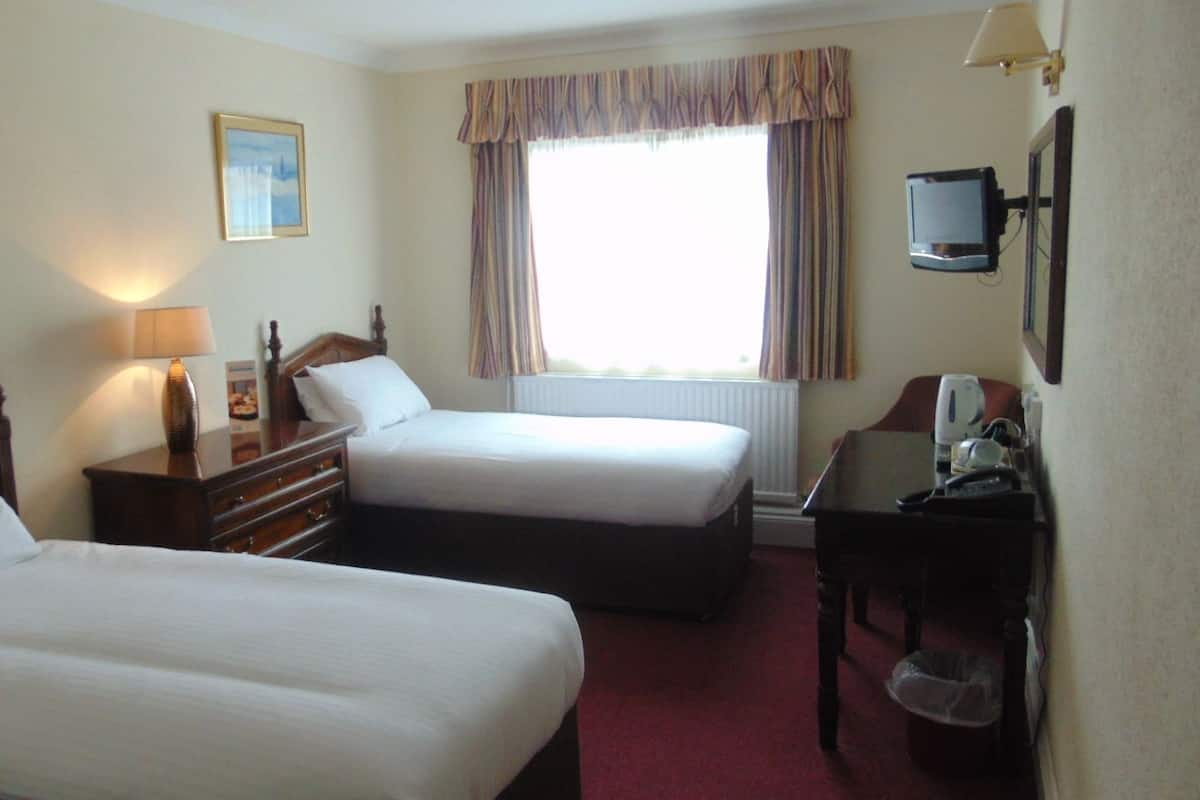 A hotel room with two single beds, a desk with a chair, a television, and a window with curtains.