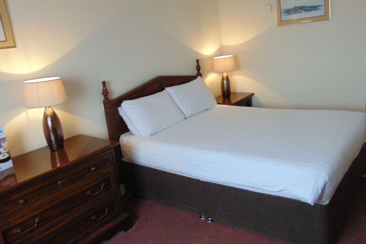A neatly made bed with white linens, a wooden headboard, and two bedside lamps on matching wooden nightstands.