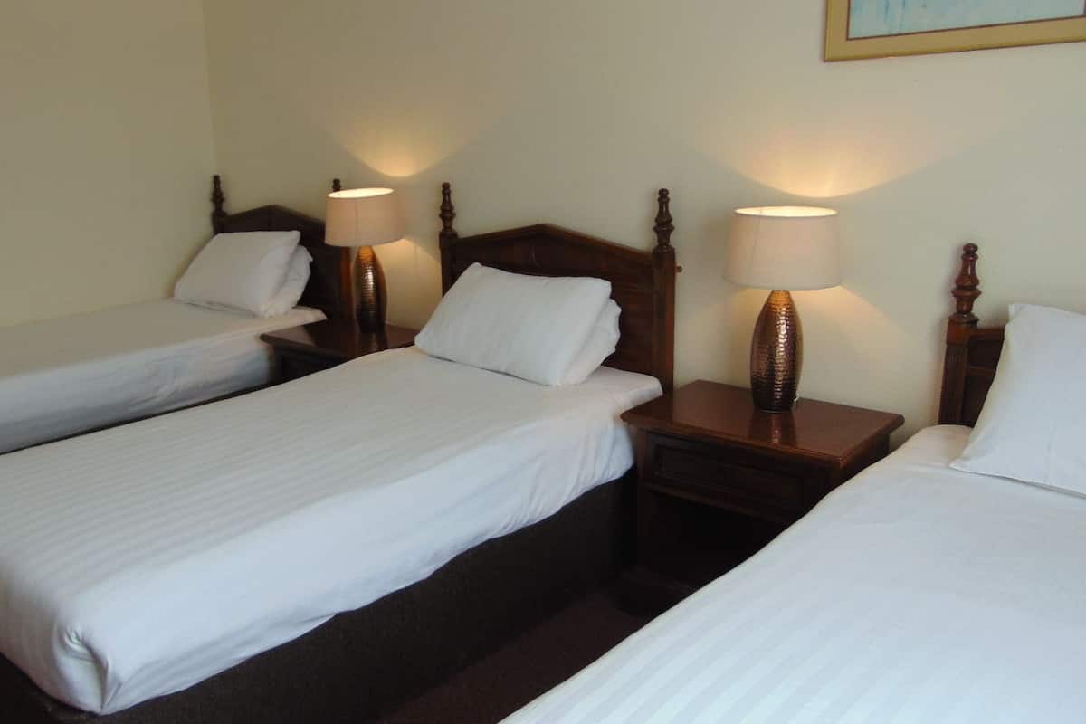 A hotel room with three single beds, wooden headboards, and bedside lamps.