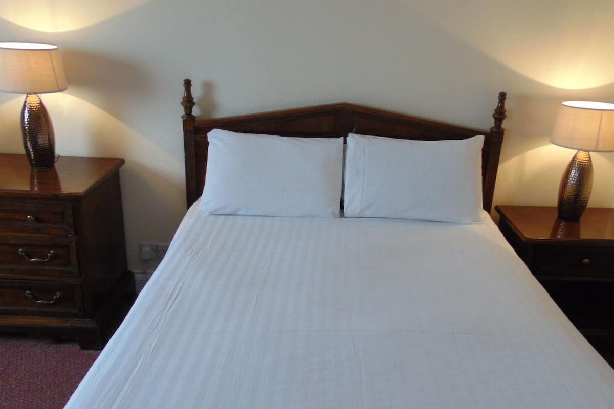 A neatly made bed with white linens, flanked by two bedside tables with lamps.