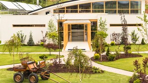 Un edificio moderno con una entrada amplia, rodeado de jardines cuidados y un carrito pequeño.