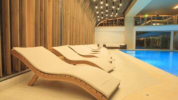 A modern indoor pool area with sun loungers and a view of the pool.