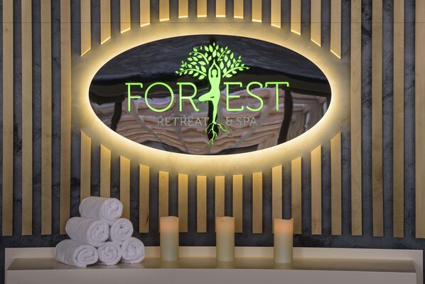 A reception area with a logo for 'FOREST RETREAT & SPA', a tree symbol, and a stack of white towels. - Forest Retreat & Spa (Oveselu)