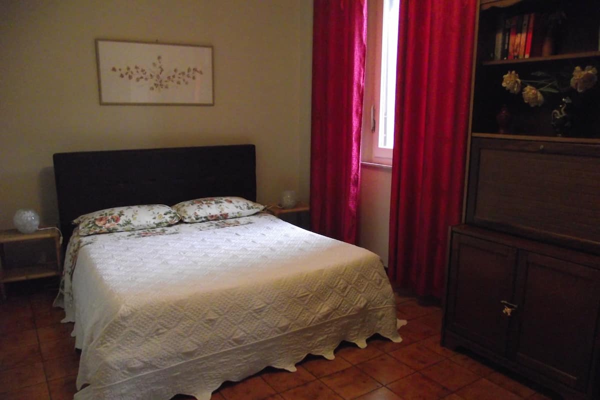 Une chambre à coucher avec un lit, une table de chevet, une commode et une fenêtre avec des rideaux rouges.