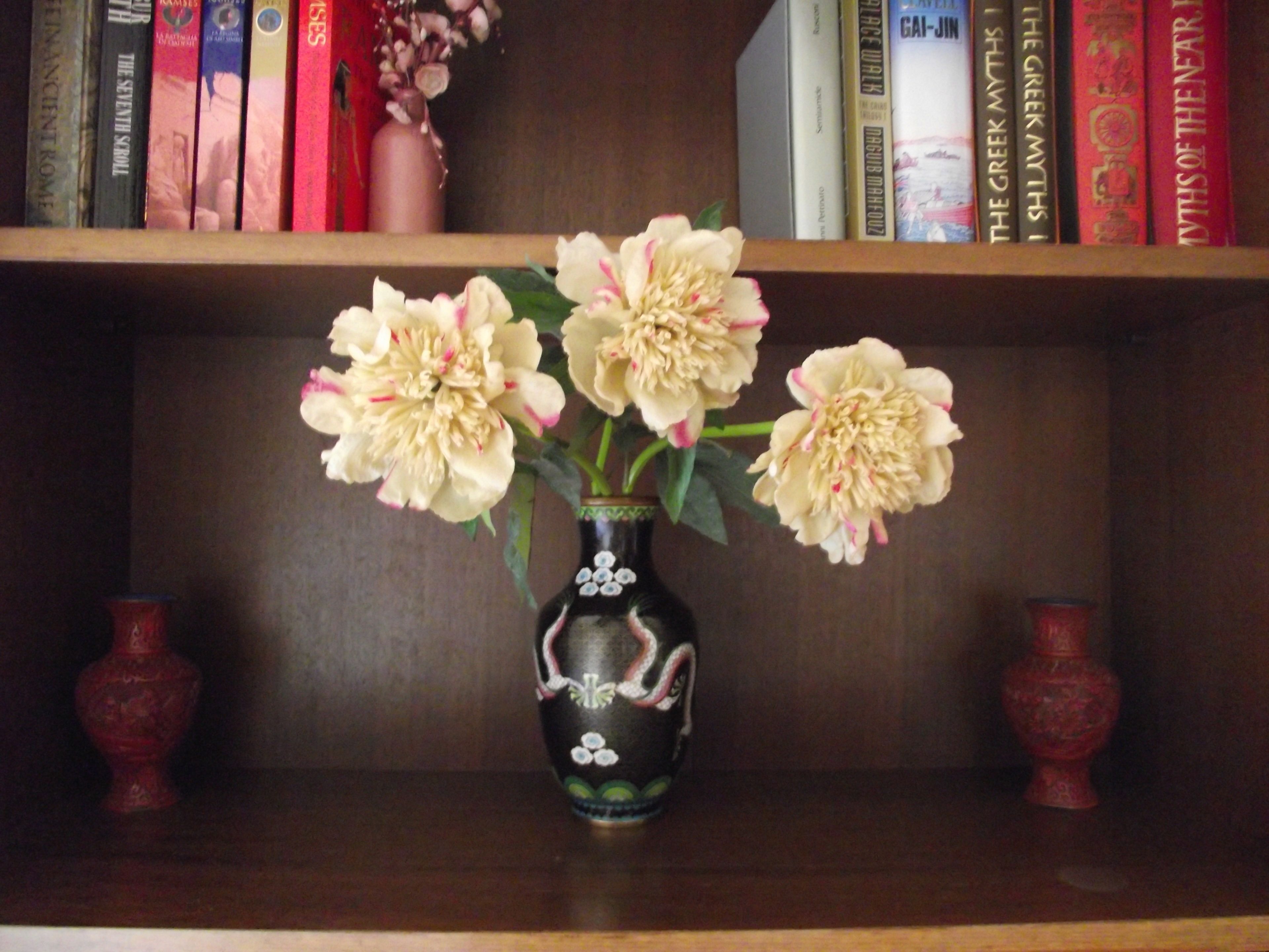 A bookshelf with books and a vase with flowers.