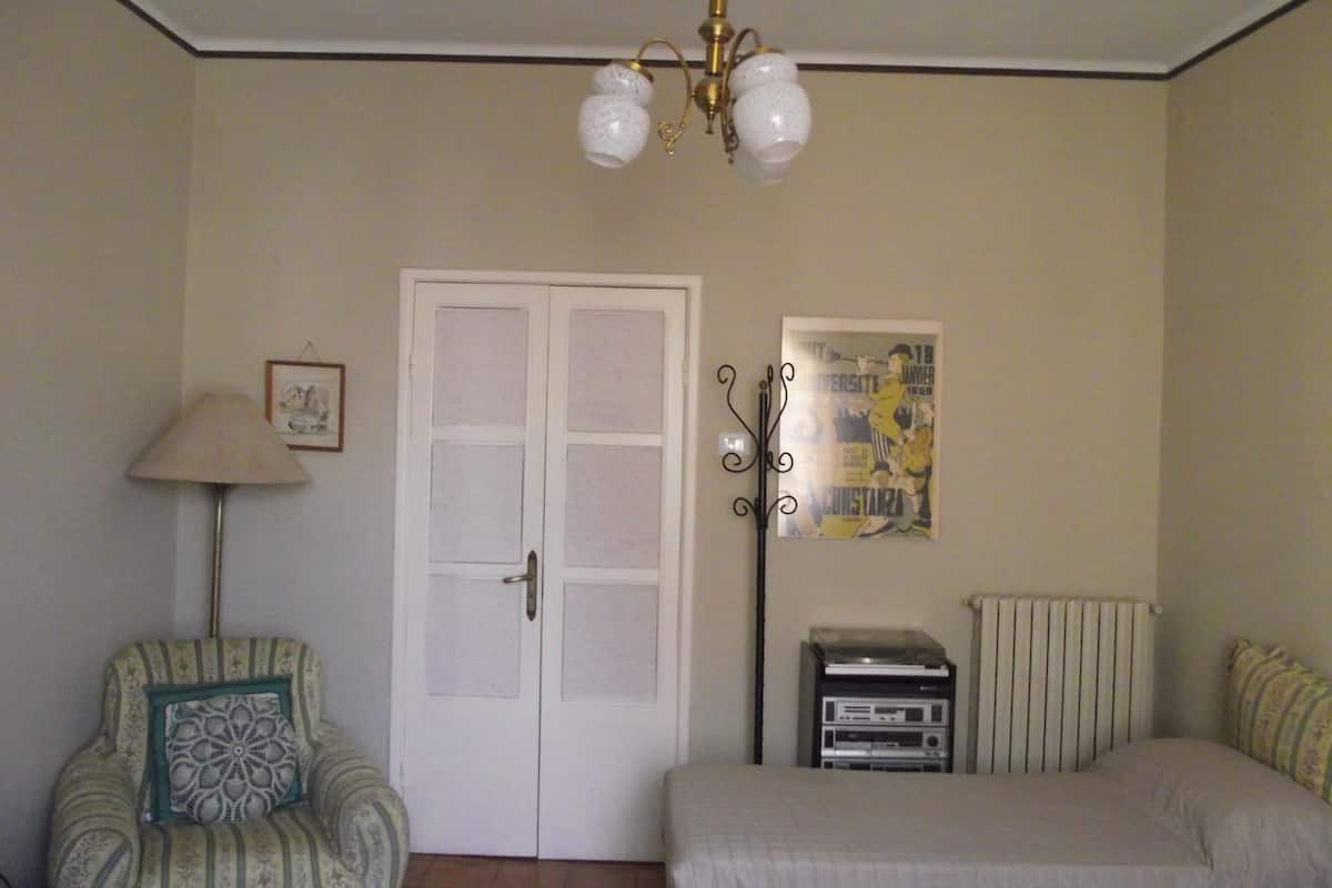 Une chambre à coucher avec un lit, une chaise, un radiateur, une affiche et une porte.
