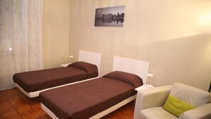 A room with two single beds, a white armchair, and a cityscape painting on the wall.
