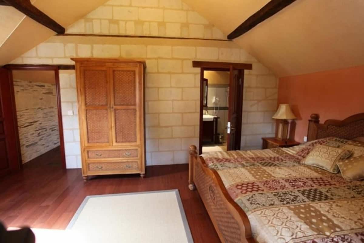 A bedroom with a wooden wardrobe, a patterned bedspread, and a wooden floor.