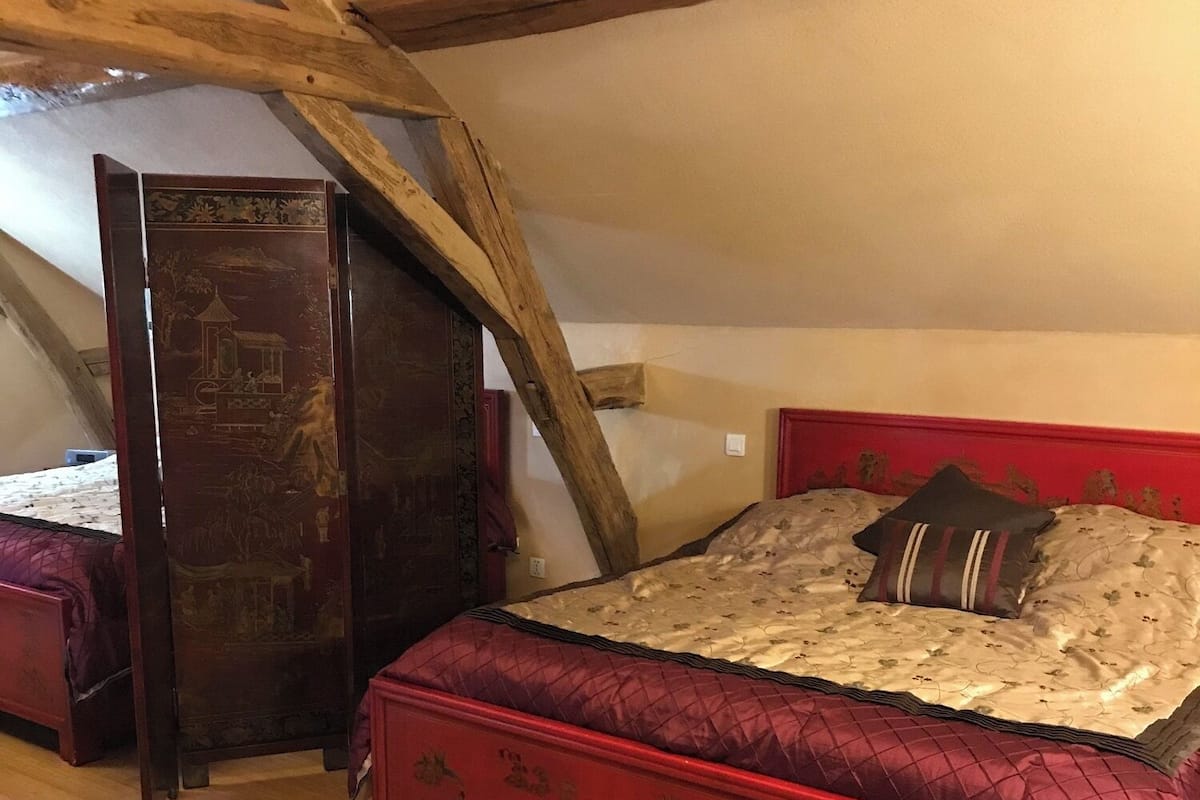 A bedroom with a wooden ceiling, a red bed with floral patterns, and a large wooden cabinet.