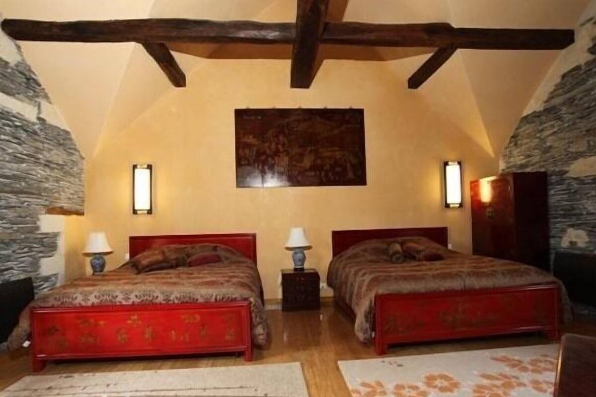 A bedroom with two beds, stone walls, wooden beams, and a painting on the wall.