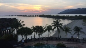 Un complexe hôtelier doté d’une piscine, de palmiers et offrant une vue sur une étendue d’eau paisible au coucher du soleil.