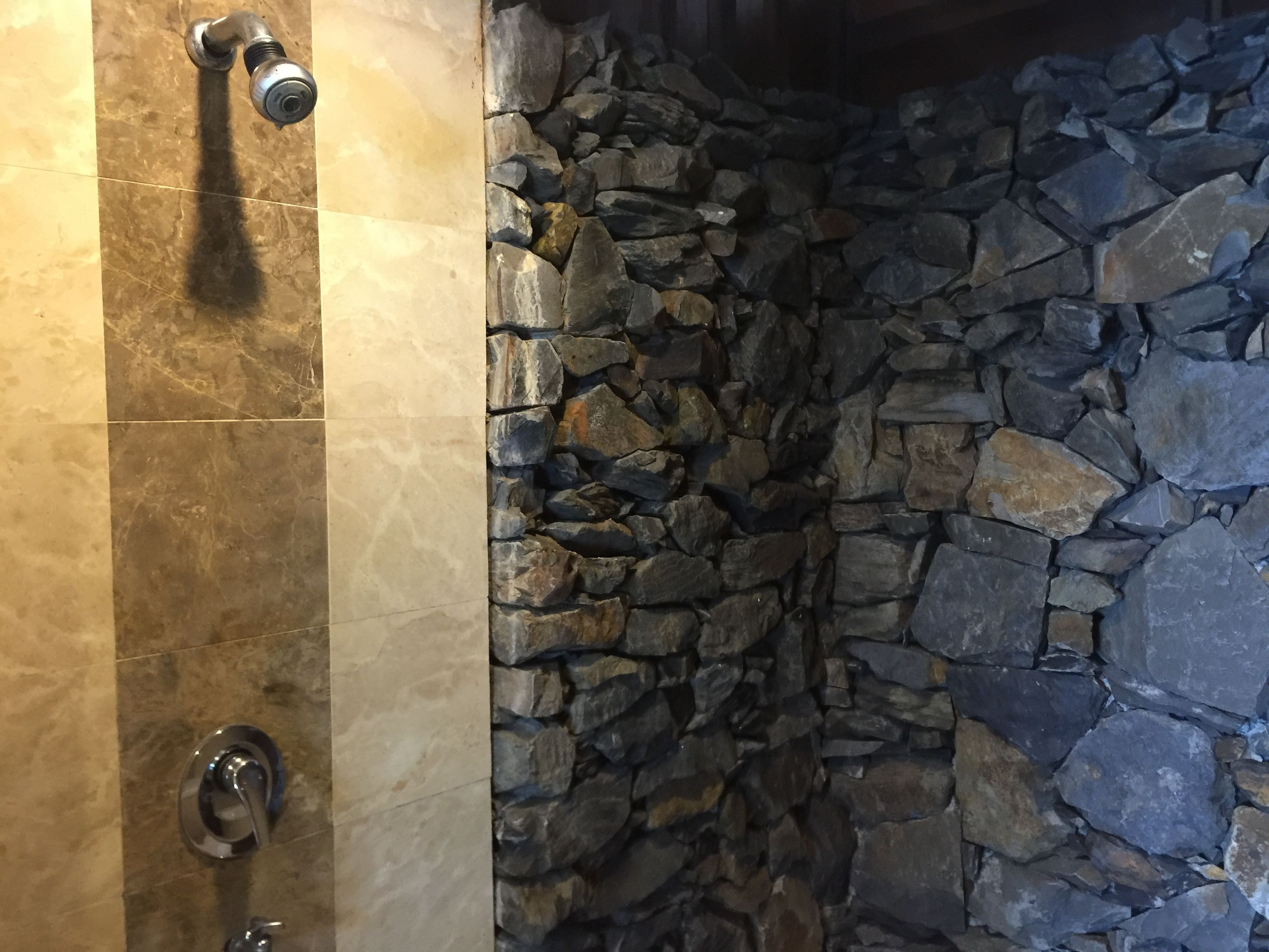 Un baño con pared de piedra y ducha con grifo cromado.