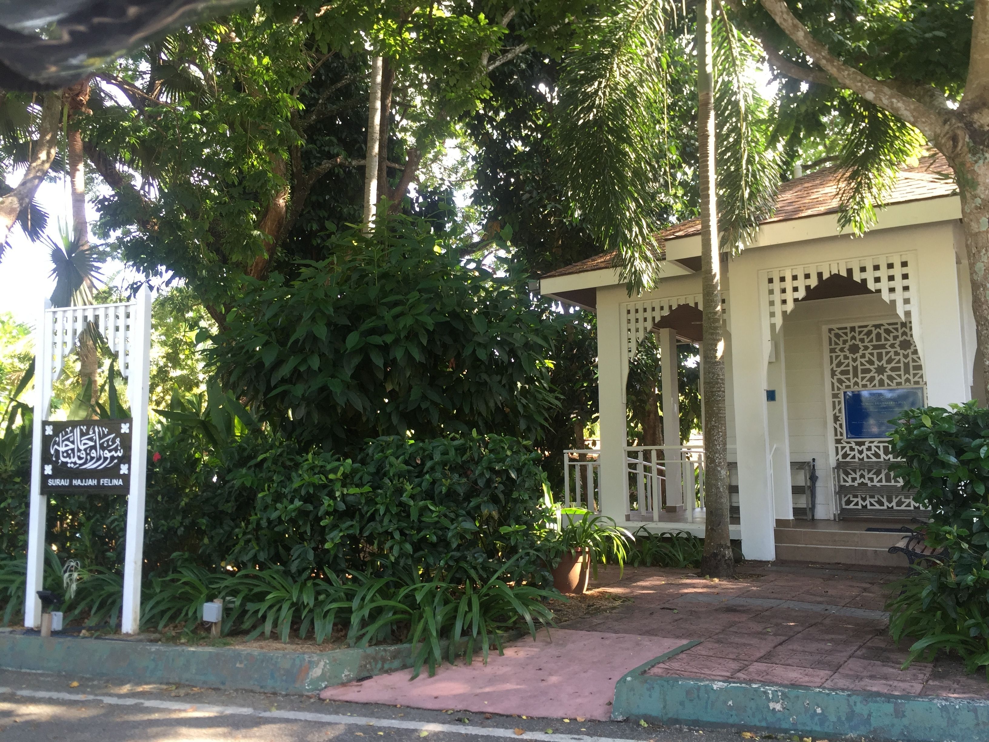A building with a covered entrance, surrounded by lush greenery and a white fence.