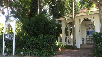 A building with a covered entrance, surrounded by lush greenery and a white fence.
