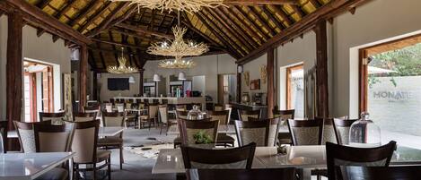 Un comedor amplio con techos altos y luz natural, que presenta mobiliario de madera y un candelabro central.
