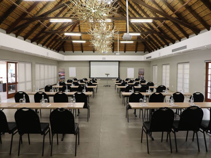 A conference room with multiple tables and chairs, a projector screen, and a large chandelier.