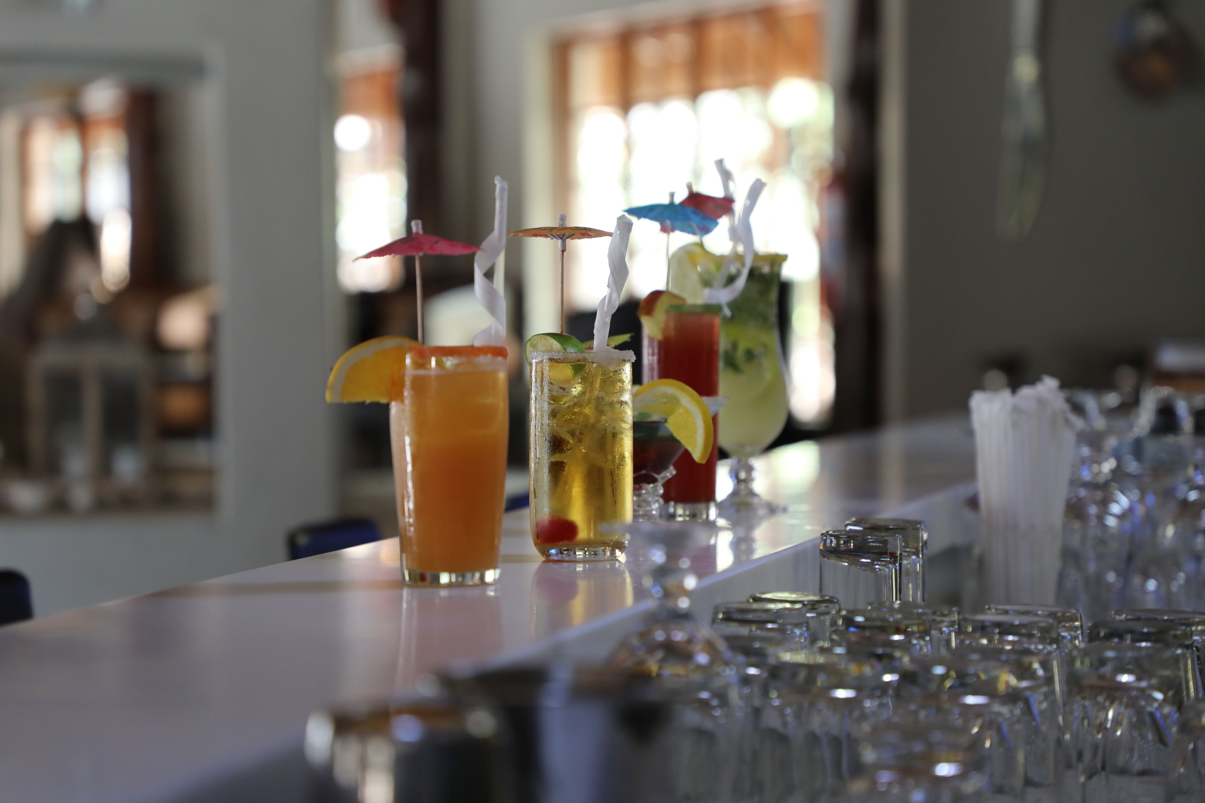 Zona de bar con varios vasos de bebidas diversas, algunas con sombrillas y pajitas.