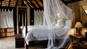 Una habitación con cama con dosel, dosel, mesita de noche con lámpara y cestas de mimbre.