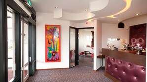 A hotel reception area with a modern design, including a large colorful abstract painting, a plush red seating area, and a patterned carpet. - Villavelo Twente (Ootmarsum)