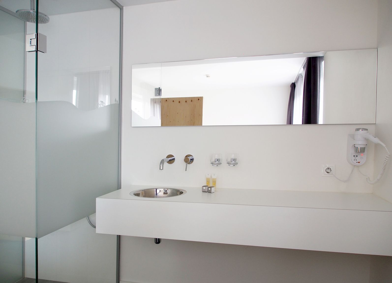 A modern bathroom with a white vanity, a large mirror, a shower, and a telephone.