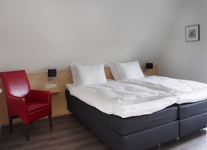 A bedroom with a bed, a red chair, a nightstand, and a wall-mounted lamp. - Villavelo Twente (Ootmarsum)