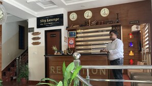 Zona de recepción de un hotel, con un letrero que indica 'Sky Lounge On Terrace' y relojes mostrando la hora.